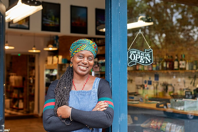 A woman business owner leaning in the doorway of her storefront.