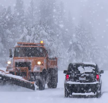 car and snow plow driving on a snowy road