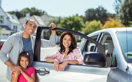 A father and mother standing by their car with their daughter.