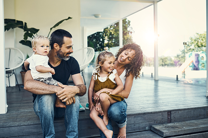 A young family laughing with their children on their house porch.